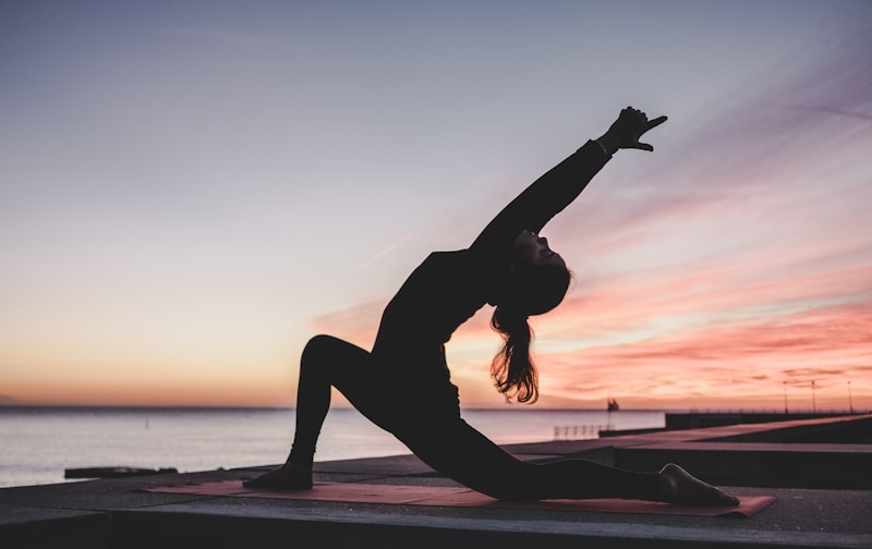 Silhouette einer Frau in Yoga-Pose auf einer Matte am Meer bei Sonnenuntergang